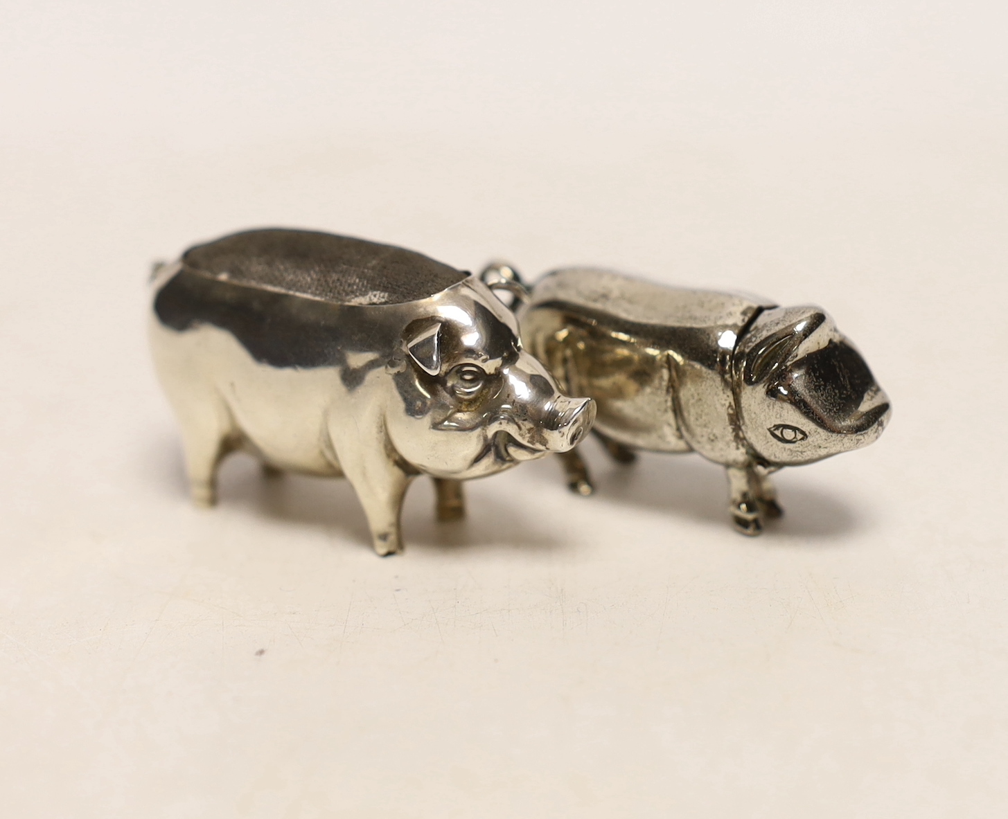 An Edwardian novelty silver pin cushion modelled as a pig, Henry Matthews, Birmingham, 1907, length 53mm, together with a metal box, modelled as a pig with hinged head.